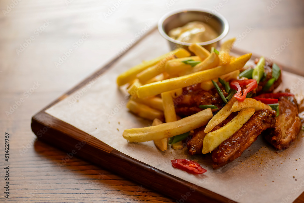 French Fries with fried chicken served with sauce on a wooden cutting board over wooden table background