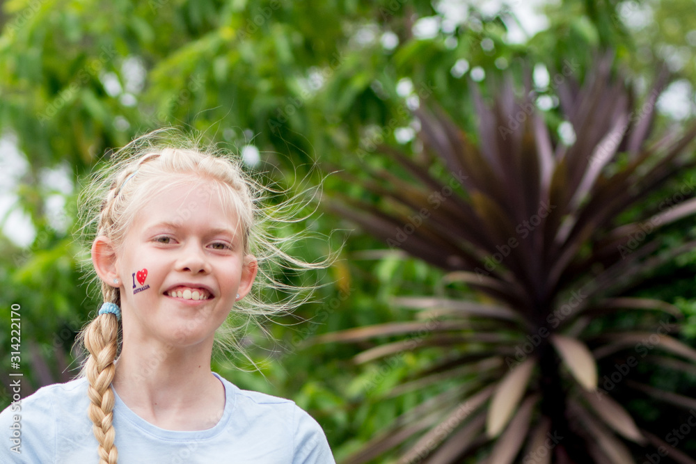 Cute caucasian blond girl with temporary tattoo -I love Australia- on her face to celebrate Australia Day on a green tree background. Empty space for text unput Cute caucasian blond girl with temporary tattoo -I love Australia- on her face to celebrate Australia Day on a green tree background. Empty space for text unput