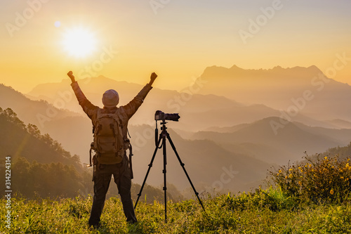 Successful people concept.Nature photographer stretching hands on peak of mountain at morning sunrise