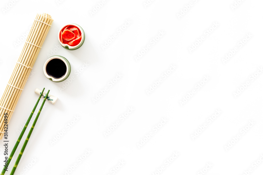 Table served for eating sushi. Chopsticks, bowls with ginger and sause, mat on white background top-down copy space Table served for eating sushi. Chopsticks, bowls with ginger and sause, mat on white background top-down copy space