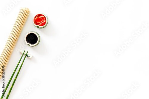 Table served for eating sushi. Chopsticks, bowls with ginger and sause, mat on white background top-down copy space © 279photo