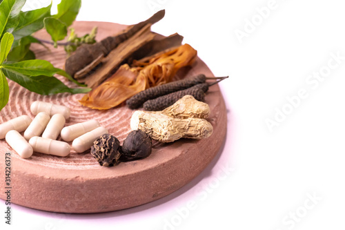 Traditional Indian medicine concept. Cinnamon, dried ginger, black cardamom, javitri, long pepper, and ayurvedic capsules with green herbs on a stone