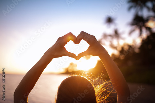 Female making a heart shape on the beach at sunset. People love, nature symbol concept.  photo