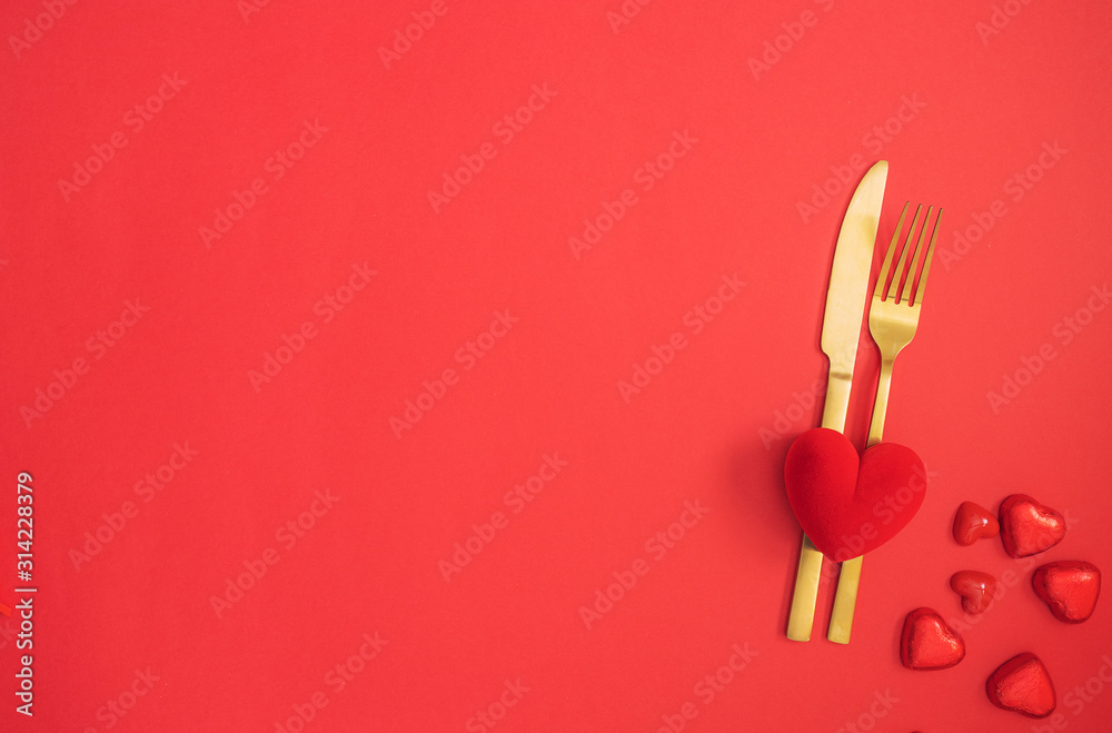 Gold cutlery and red heart on red background. Saint Valentines day celebration or romantic dinner minimal concept. Gold cutlery and red heart on red background. Saint Valentines day celebration or romantic dinner minimal concept.