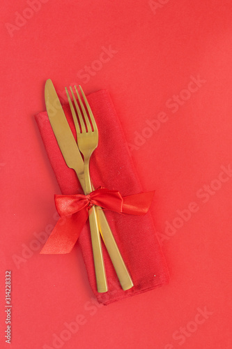 Gold cutlery on red background . Saint Valentines day celebration or romantic dinner minimal concept.