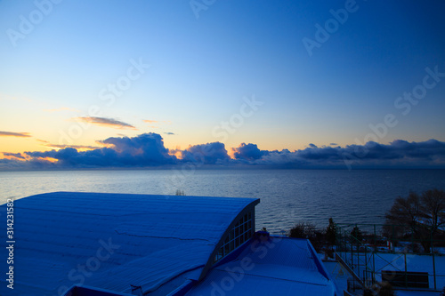 Winter beach. Dawn over the lake. Roofs of houses. View from the window