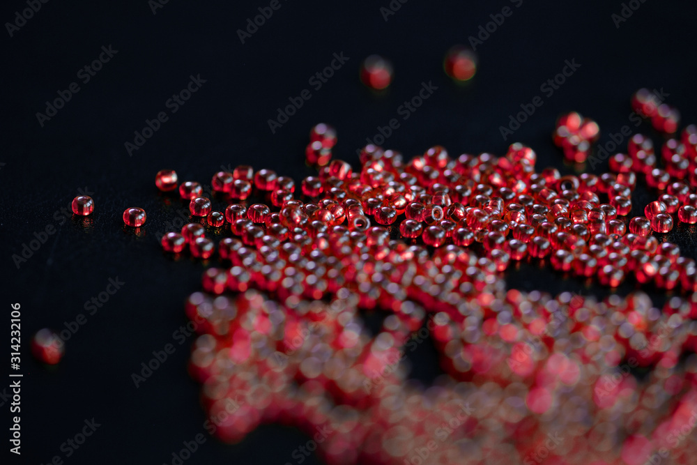 Transparent seed beads red color scattered on a dark background close-up Transparent seed beads red color scattered on a dark background close-up