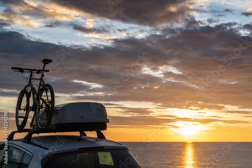 Mounted bicycle silhouette on the car roof with rising sun background. Dramatic sky at mediterranean sea dawn.