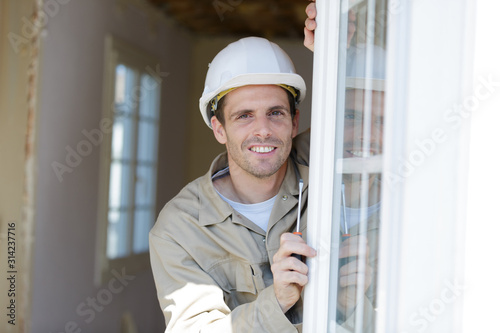 male builder with a screwdriver sets fittings on the window