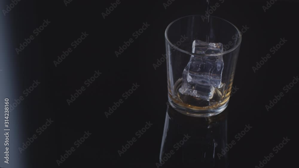 large plan in a glass with two ice cubes pour whiskey on a black background large plan in a glass with two ice cubes pour whiskey on a black background
