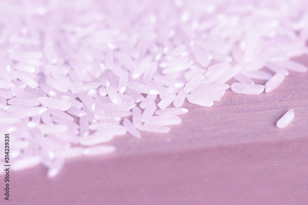 Obraz premium White rice grains scattered on a wooden surface close up. Food background