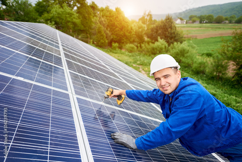 Construction worker connects photo voltaic panel to solar system using screwdriver. Professional installing and construction of solar system, looking to the camera. Alternative energy concept