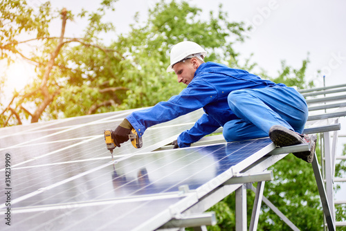 Young construction worker connects photo voltaic panel to solar system using screwdriver on bright sunny day. Alternative cheap sun energy production and profitable financial investment concept.