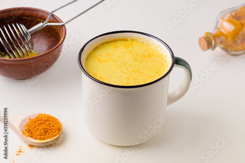 golden milk in a mug on a white table in the cooking process.