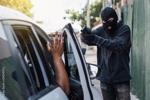 A thief  is trying to steal a car, holding a pointed gun in a car driver, hijacking