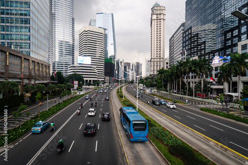 Transjakarta bus drive in its dedicated traffic lane in the modern financial district of Jakarta in Indonesia capital city with an overcast sky photo