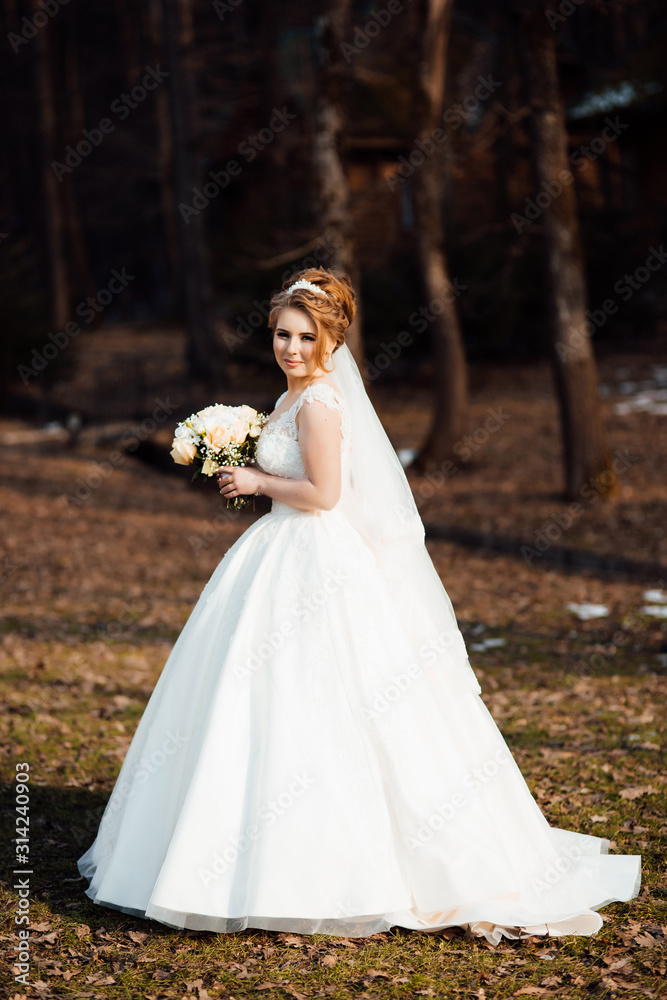 Beautiful luxury bride in elegant white dress. Gorgeous beautiful bride smiles while posing with bouquet. Beautiful stylish bride with bouquet in hand