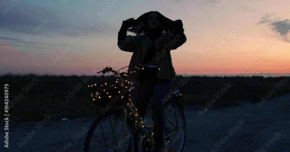 Sagoma di una ragazza cammina su una bicicletta la sera al tramonto.