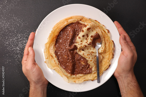 crepe with chocolate sauce in plate with man hand- top view