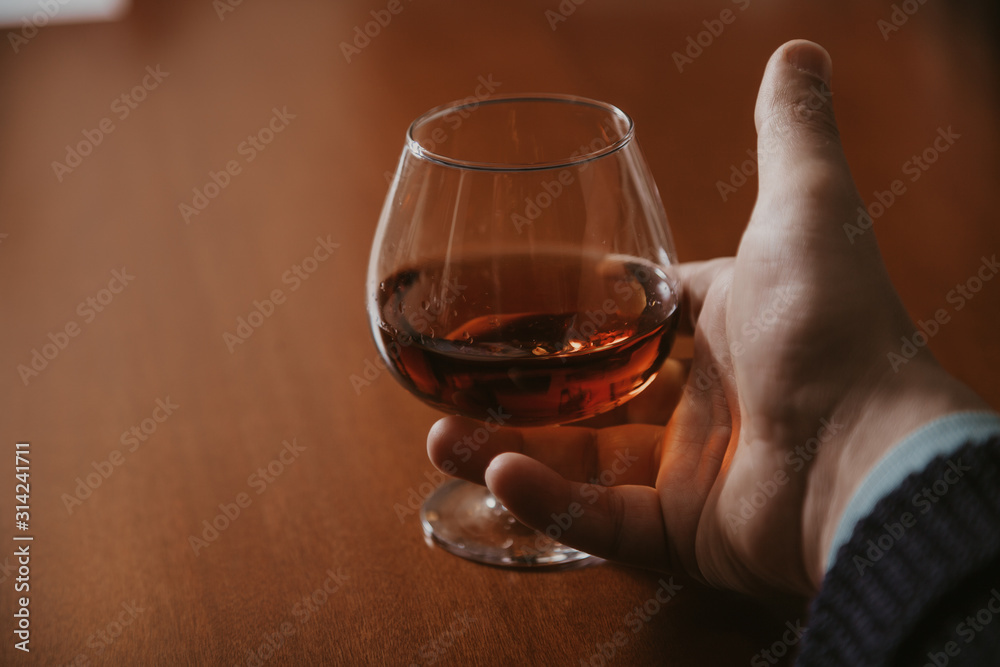 Hand holds glass with cognac close-up Hand holds glass with cognac close-up