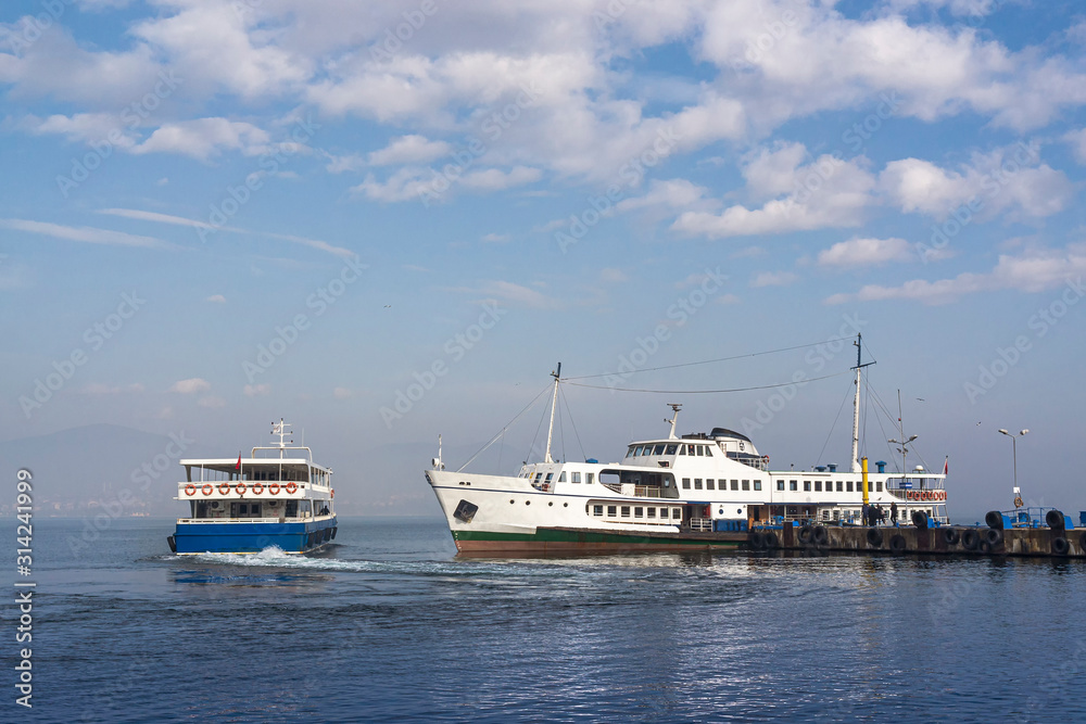 Two passenger ferries at the pier in Degirmendere/Kocaeli, Marmara sea, Turkey. Sunny winter day, calm water, blue sky with beautiful white clouds