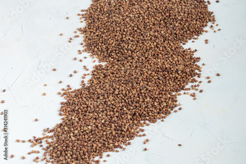 Buckwheat groats are scattered on a light background. Dark texture and background.