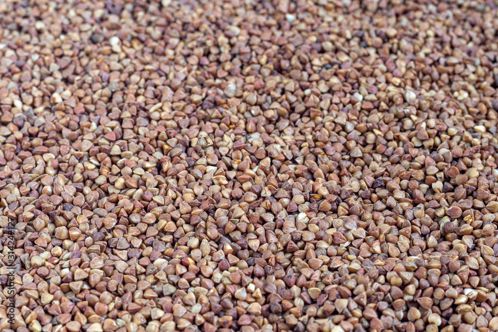 Buckwheat groats are scattered on a light background. Dark texture and background. Buckwheat groats are scattered on a light background. Dark texture and background.