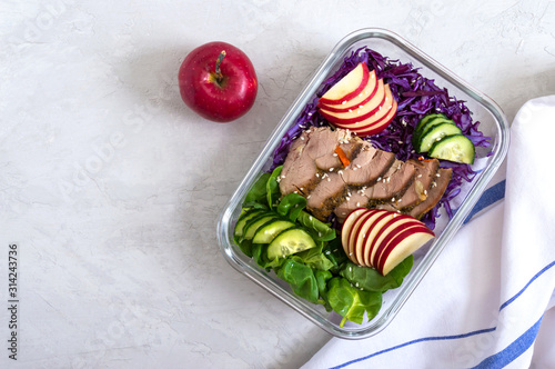 Tasty healthy lunch of vegetables and baked turkey. Salad of red cabbage, spinach, apples, fresh cucumbers with diet meat in a glass lunchbox. Sports diet. Proper nutrition.