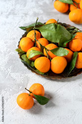 Fresh mandarin oranges fruit or tangerines with leaves in an iron tray on a gray background © teleginatania
