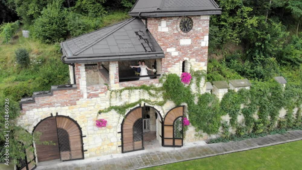 Brides in a small castle are standing next to each other, hugging. Newlyweds on the balcony of a magnificent castle, which is overgrown with hedges Brides in a small castle are standing next to each other, hugging. Newlyweds on the balcony of a magnificent castle, which is overgrown with hedges