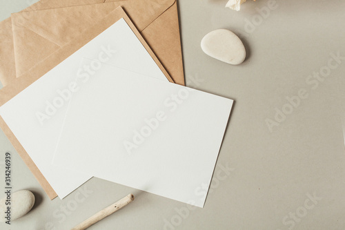 Blank paper sheets with empty copy space for text, envelopes, hydrangea flower, stones on beige background. Flat lay, top view mail letter invitation.