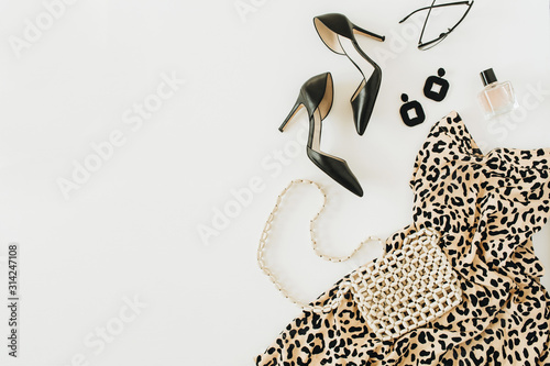Modern fashion collage with female clothes and accessories. Leopard print dress, high-heel shoes, earrings, glasses, purse, perfume on white background. Flat lay, top view.