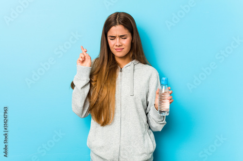 Young fitness woman holding a water bottle crossing fingers for having luck © Asier