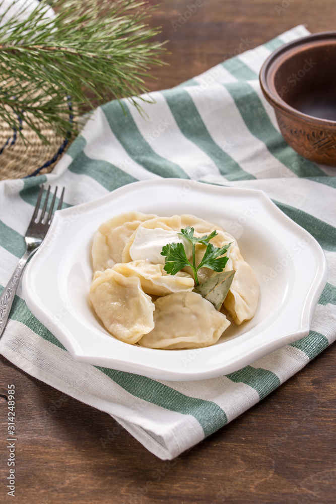 Russian meat dumplings pelmeni with sour cream on white plate on wooden table