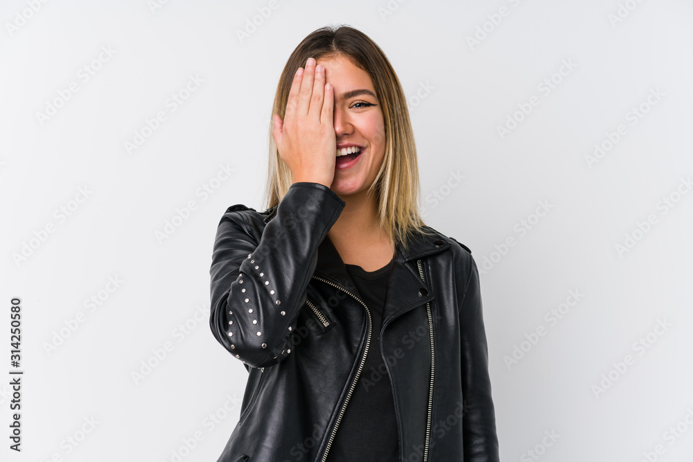 Young caucasian woman wearing a black leather jacket having fun covering half of face with palm.