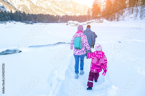 Winter landscape with family people walking on a frozen river or lake in the Altai mountains on a sunny day under a blue sky with snowdrifts around.