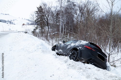 Accident on a winter snowy track with a black car skidding and falling into a ditch due to ice. Safety and poor driving on the road.