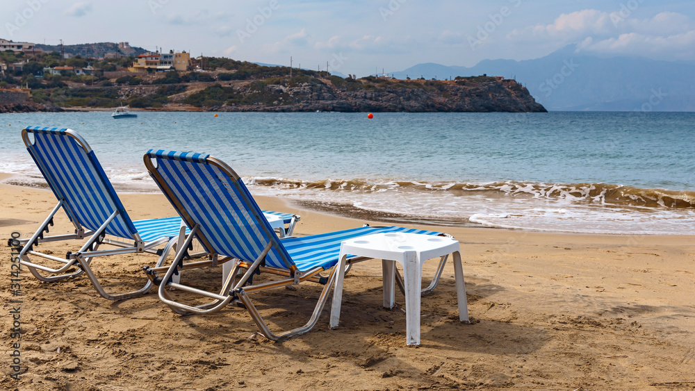 two sun loungers on the sandy beach of the Greek resort town of Agios Nikolaos