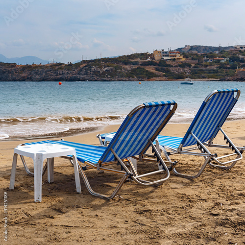 two sun loungers on the sandy beach of the Greek resort town of Agios Nikolaos © westermak15