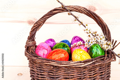 Hand-painted easter eggs in rainbow colors in a basket on a wooden background, decorated with cherry blossom. Springtime holidays concept