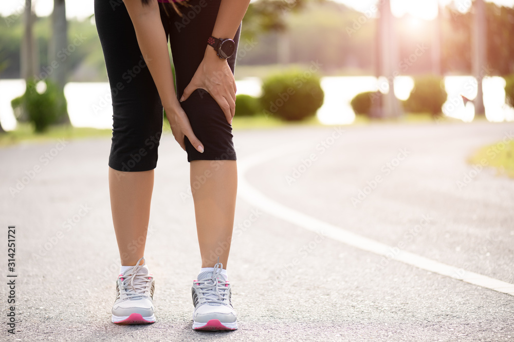 Young fitness woman runner feel pain on her knee in the park. Outdoor exercise activities concept.