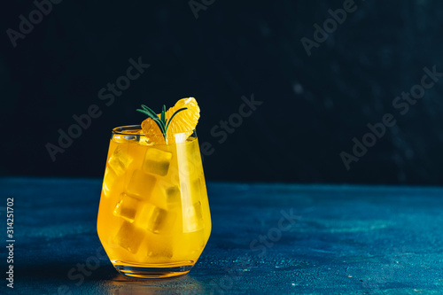 Yellow orange cocktail with tangerine and rosemary with ice in glass on dark blue concrete background , close up. Christmas and New Year holiday welcome drink