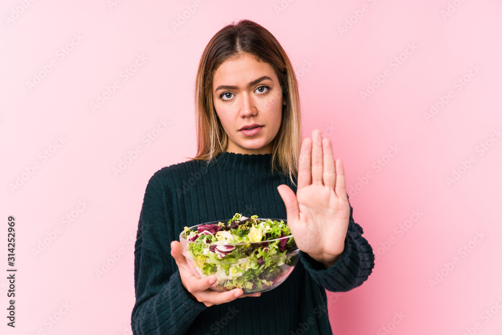 Young caucasian woman holding a salad isolated standing with outstretched hand showing stop sign, preventing you.