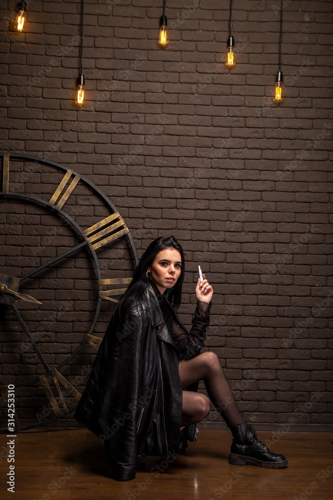 Naklejka premium brunette in a black leather jacket on a background of a brown brick wall and a clock