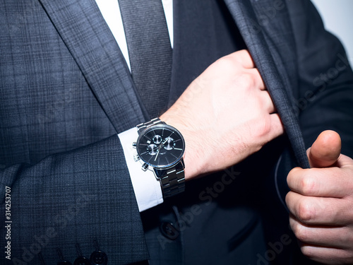 men suit perfect to the last detail.Man posing in black suit.closeup fashion image of luxury watch on wrist of man.body detail of a business man.Man's hand in a grey shirt with cufflinks.