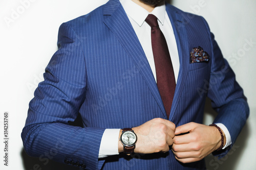 Closeup fashion image of luxury watch on wrist of man.body detail of a business man.Man's hand in blue pants pocket closeup at white background.Man wearing blue jacket and white shirt.Not isolated