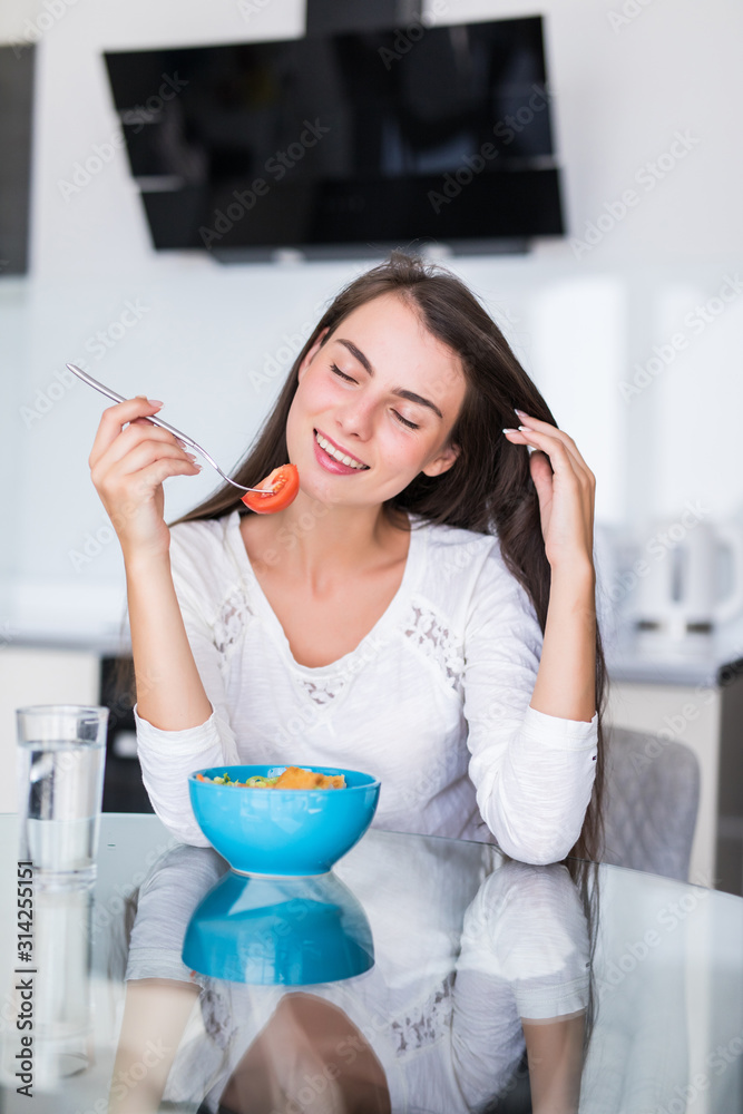 Smiling woman eating a salad in kitchen Smiling woman eating a salad in kitchen
