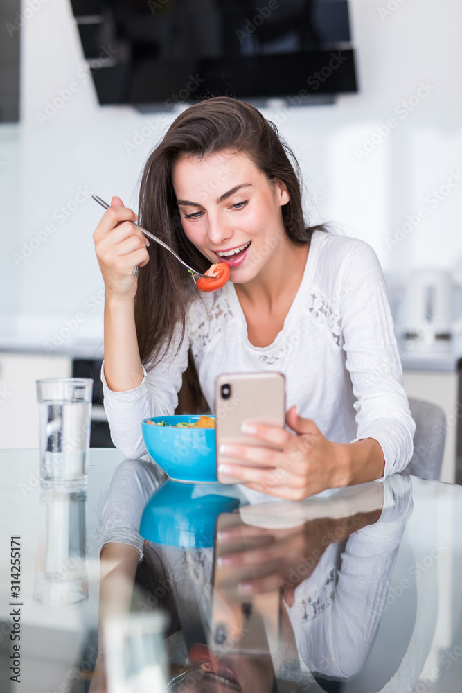 Beautiful young woman using cell phone while making salad in the kitchen. Healthy food. vegetable salad. Diet. Healthy lifestyle. Cooking at home. Beautiful young woman using cell phone while making salad in the kitchen. Healthy food. vegetable salad. Diet. Healthy lifestyle. Cooking at home.