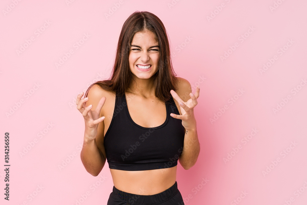 Young caucasian fitness woman doing sport isolated upset screaming with tense hands.