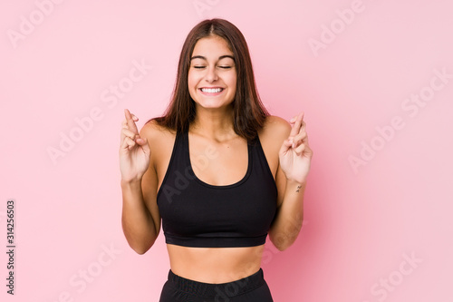 Young caucasian fitness woman doing sport isolated crossing fingers for having luck